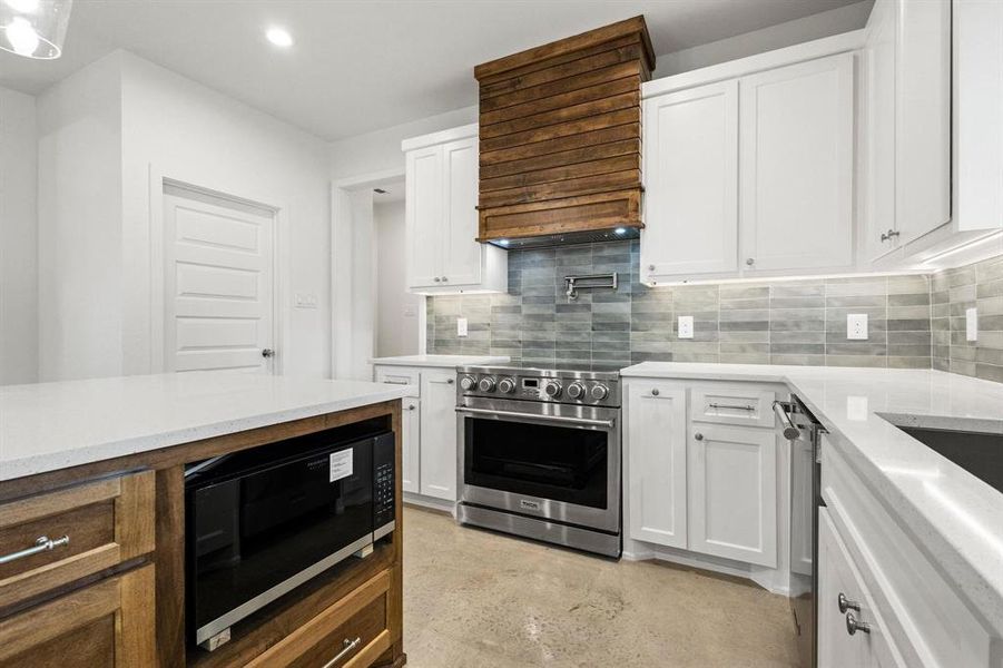 Kitchen with white cabinets, appliances with stainless steel finishes, decorative backsplash, light stone counters, and recessed lighting