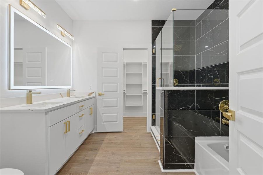Bathroom featuring a dual vanity with white cabinetry, gold-finish hardware, and a large backlit mirror