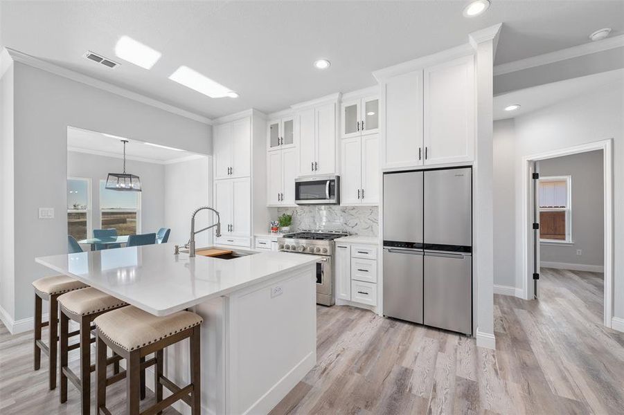 Kitchen with appliances with stainless steel finishes, white cabinetry, an island with sink, sink, and a kitchen breakfast bar