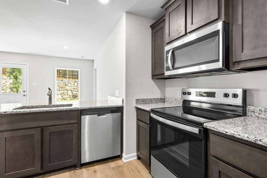 Kitchen with appliances with stainless steel finishes, dark brown cabinets, light wood-style floors, light stone counters, and recessed lighting