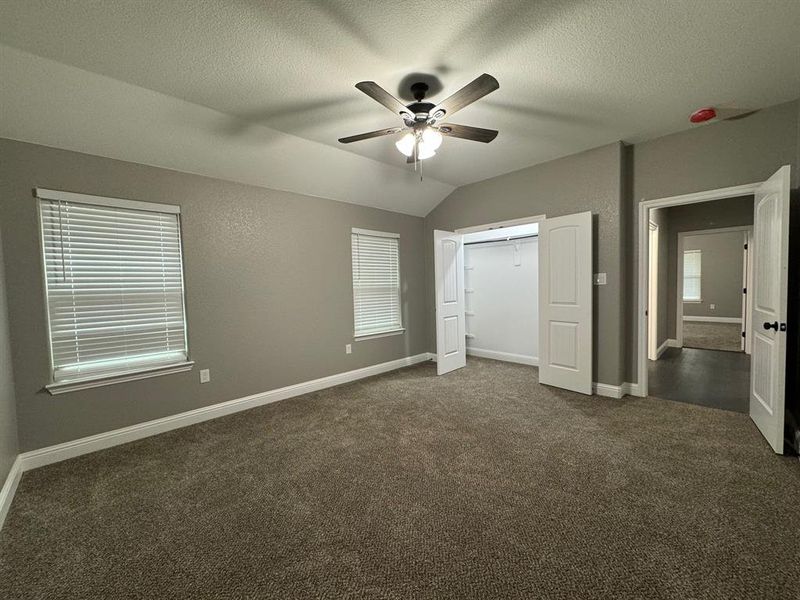 Unfurnished bedroom featuring ceiling fan, dark colored carpet, a textured ceiling, lofted ceiling, and a closet