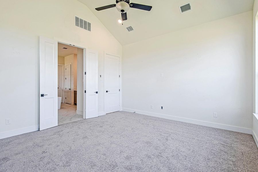 The primary suite features plush carpet, a ceiling fan, and serene backyard views