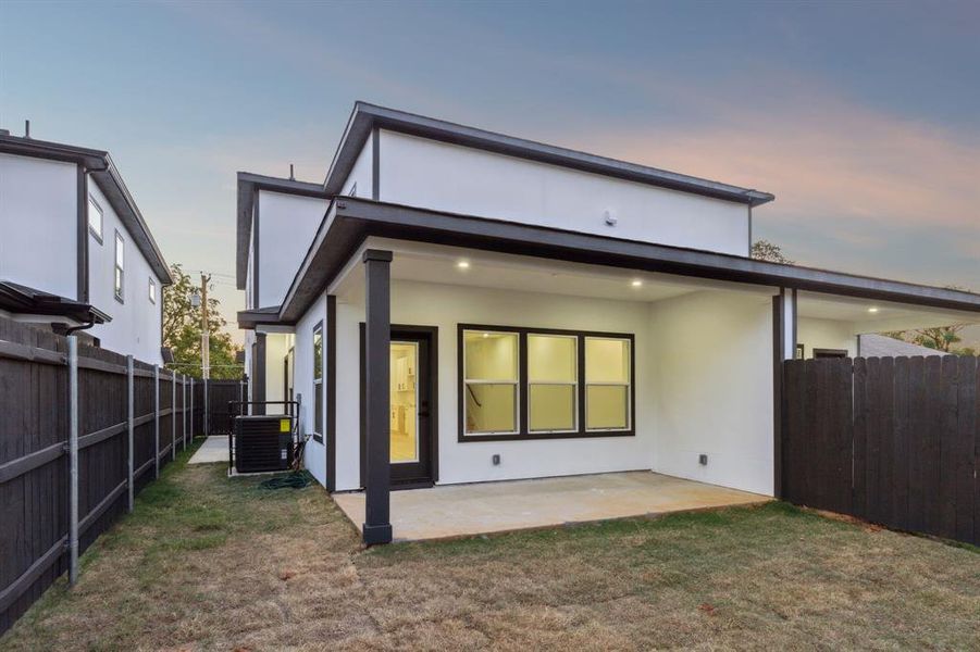 Back house at dusk featuring a yard, a patio area, and central AC