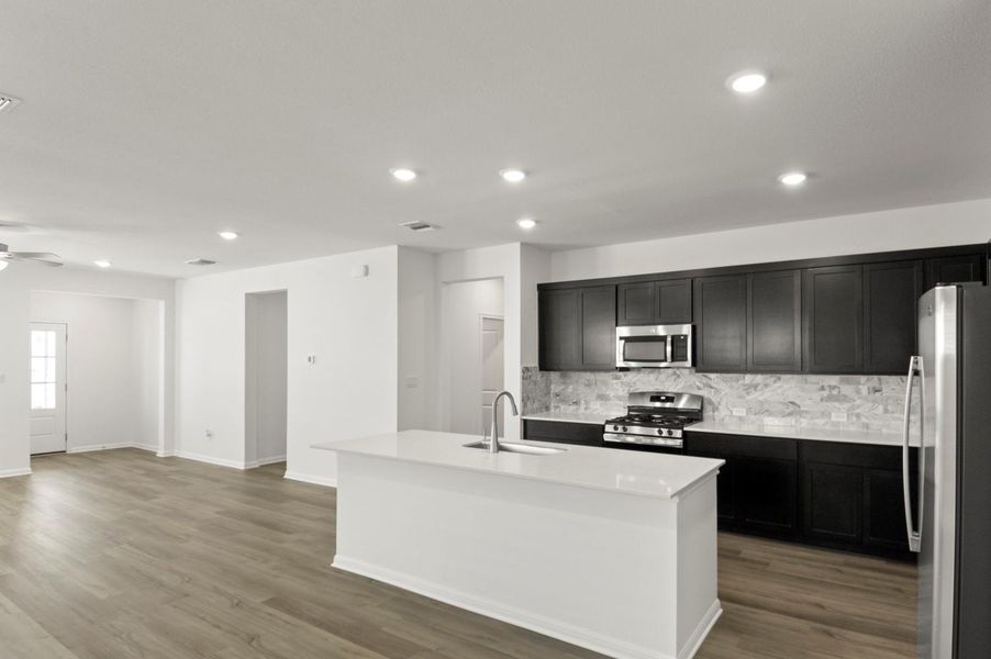 Kitchen featuring stainless steel appliances, an island with sink, backsplash, dark wood finished floors, and recessed lighting