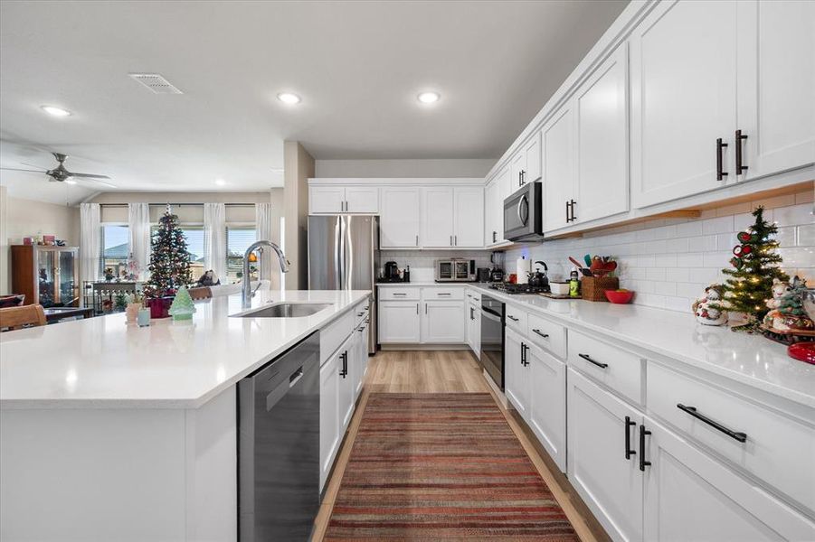 Kitchen with appliances with stainless steel finishes, white cabinets, a large island with sink, light wood-style floors, and light stone countertops Kitchen with appliances with stainless steel finishes, white cabinets, a large island with sink, light wood-style floors, and light stone countertops