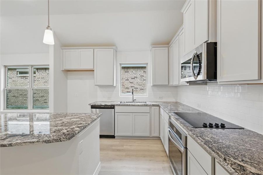 Kitchen with light wood-style floors, light stone counters, stainless steel appliances, white cabinetry, and tasteful backsplash