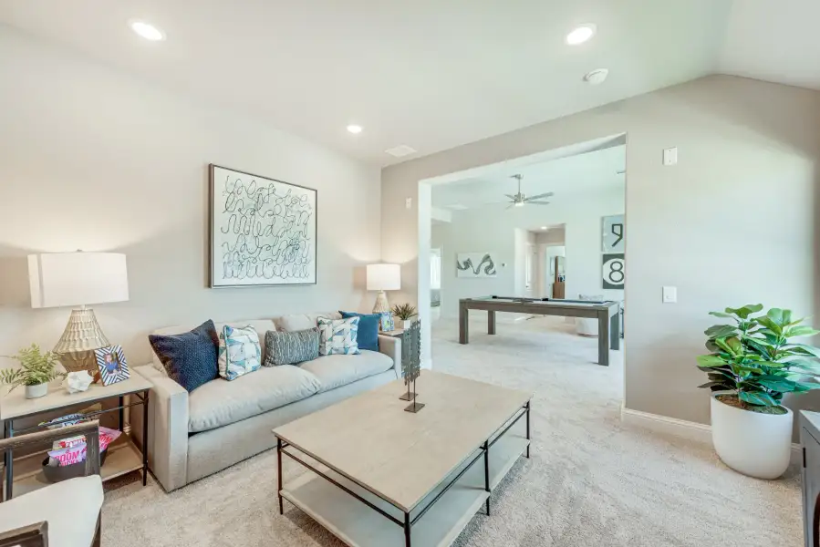 Carpeted living room with gray sofa and coffee table, open to game room with pool table beyond