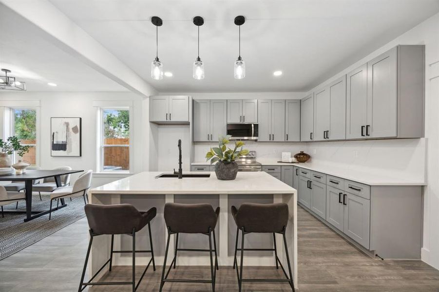 Kitchen with gray cabinetry, a center waterfall island with sink, stainless steel appliances and a pantry