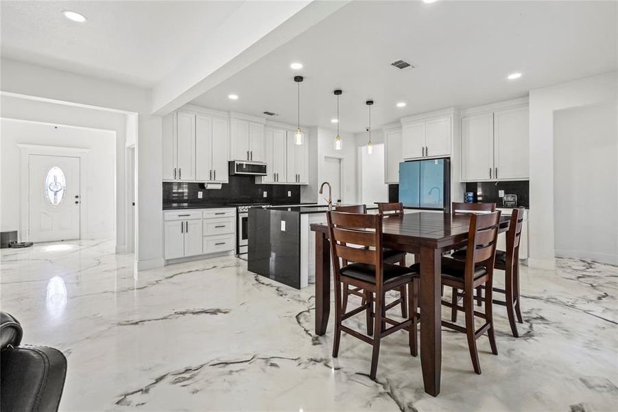 Kitchen with an island with sink, decorative backsplash, white cabinetry, decorative light fixtures, and appliances with stainless steel finishes Kitchen with an island with sink, decorative backsplash, white cabinetry, decorative light fixtures, and appliances with stainless steel finishes