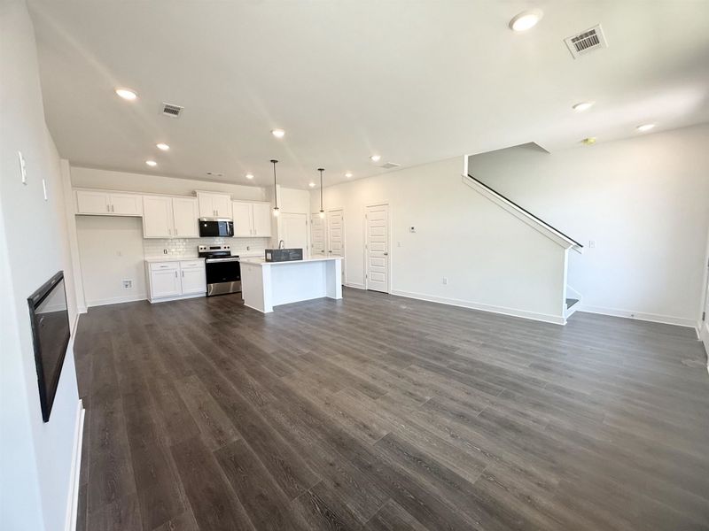 Spacious open-concept living area featuring wood-finish flooring, recessed lighting, and a modern kitchen