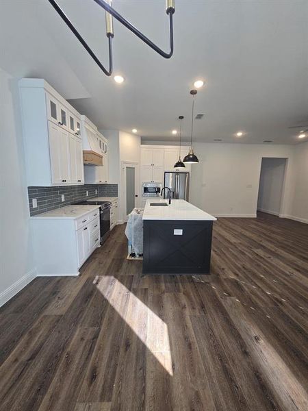Kitchen featuring white cabinetry, open floor plan, a kitchen island with sink, glass insert cabinets, and backsplash