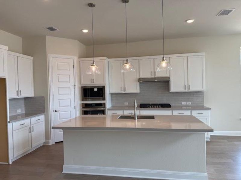 Kitchen with wood finished floors, tasteful backsplash, light countertops, white cabinetry, and recessed lighting Kitchen with wood finished floors, tasteful backsplash, light countertops, white cabinetry, and recessed lighting