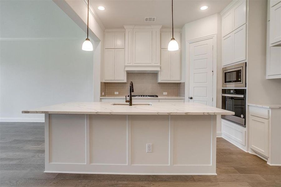 Kitchen featuring oven, light hardwood / wood-style flooring, stainless steel microwave, and decorative light fixtures