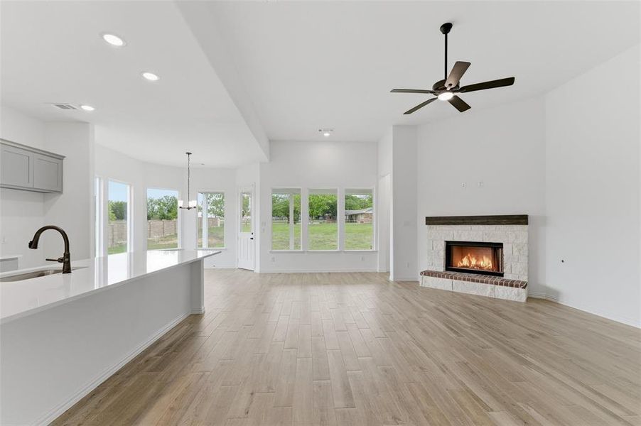 The spacious living area features light-colored flooring, a corner fireplace with a stone surround, and a ceiling fan with integrated lighting