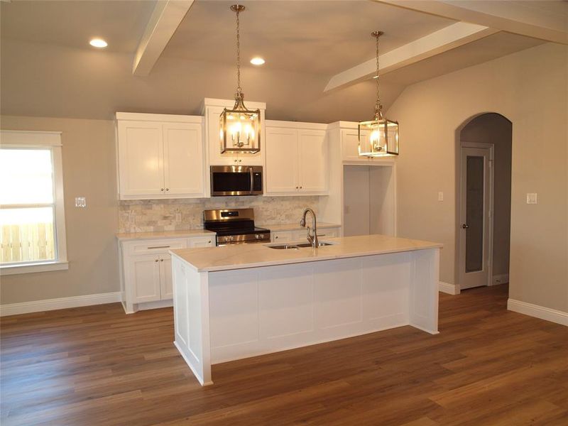 Kitchen with sink, white cabinetry, tasteful backsplash, stainless steel appliances, and a kitchen island with sink