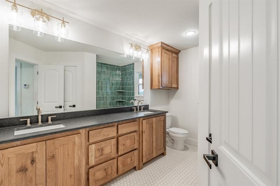 Bathroom featuring double vanity, toilet, and tiled shower