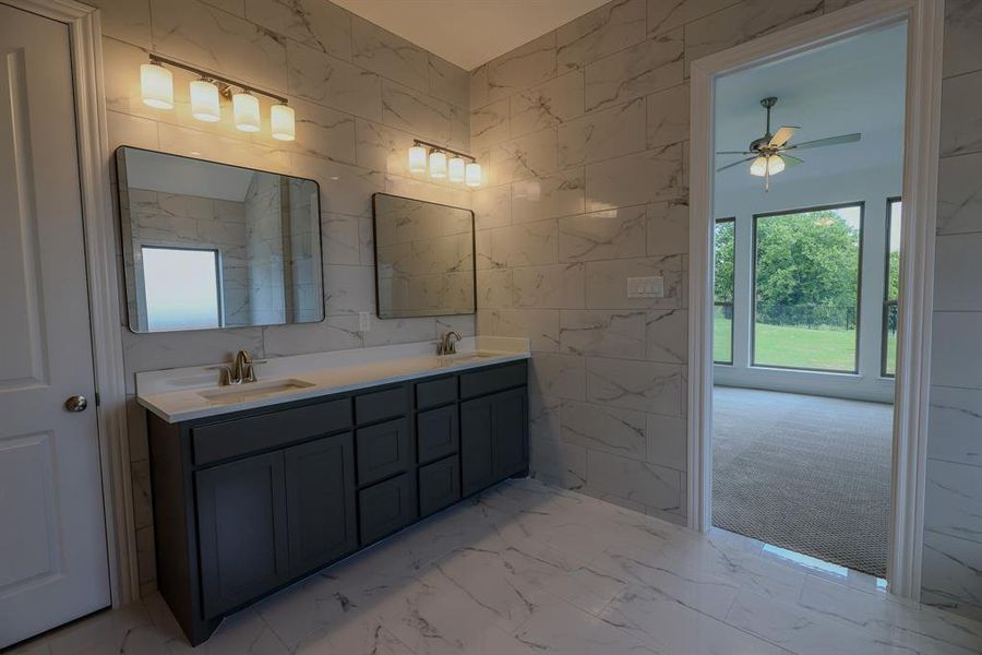 Bathroom featuring ceiling fan, marble finish floors, double vanity, and tile walls