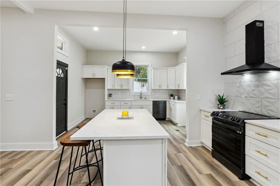 Kitchen featuring a center island, wall chimney exhaust hood, black appliances, decorative light fixtures, and backsplash