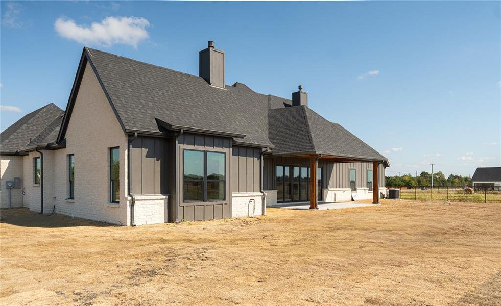 Rear view of house featuring board and batten siding, a chimney, a patio area, and roof with shingles