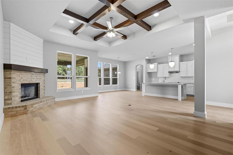 Unfurnished living room featuring coffered ceiling, arched walkways, a ceiling fan, a brick fireplace, and light wood finished floors