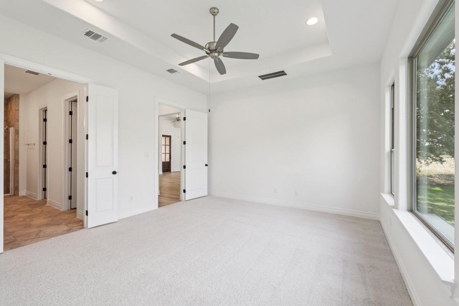 Unfurnished bedroom with a raised ceiling, light carpet, recessed lighting, and a ceiling fan