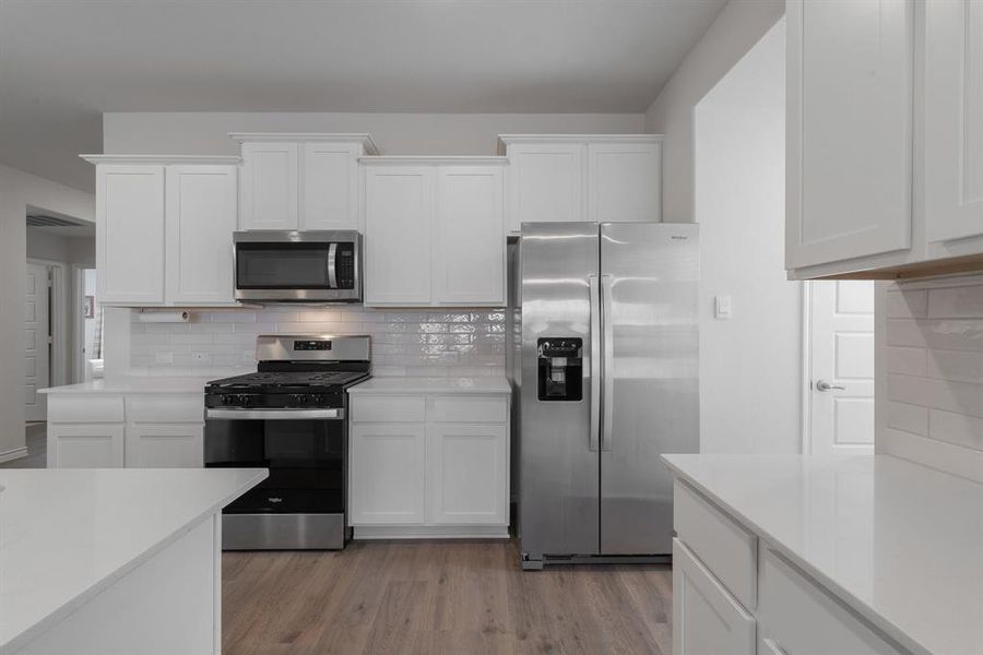 Kitchen with stainless steel appliances, white cabinets, light wood finished floors, light countertops, and tasteful backsplash