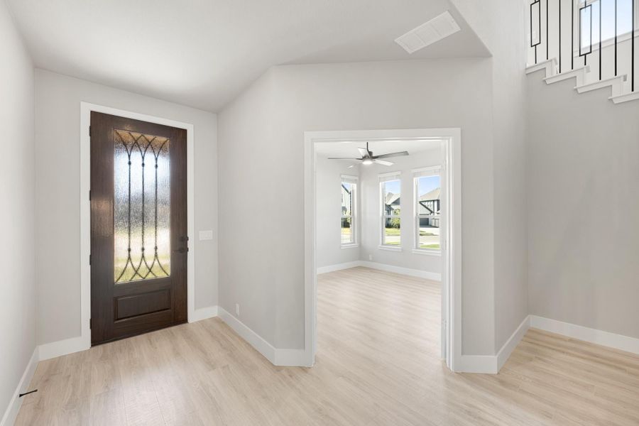 Entryway with dark wood front door featuring decorative glass panel and light hardwood floors leading to adjacent room