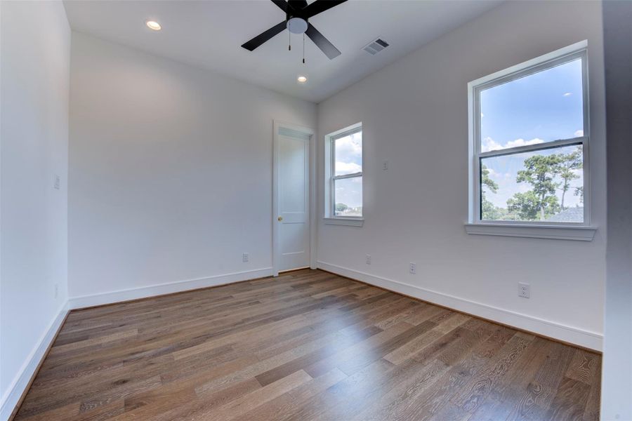 Secondary bedroom on the third level, complete with a modern ceiling fan, hardwood floors, an en-suite bathroom, and a closet.