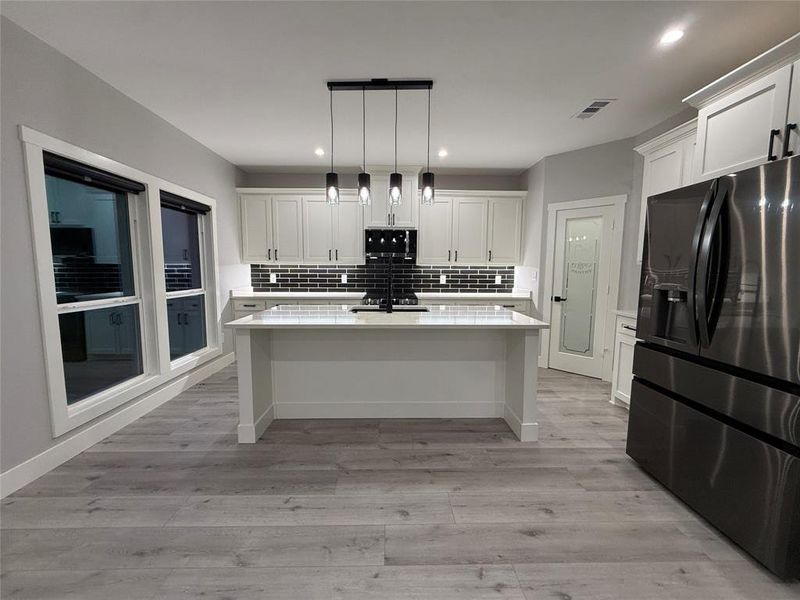 Kitchen with fridge with ice dispenser, pendant lighting, a center island with sink, white cabinets, and a breakfast bar area