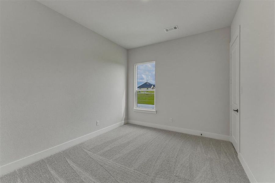 Bright room featuring a single window, light gray carpet flooring, white baseboards, and a white paneled door with a black handle Bright room featuring a single window, light gray carpet flooring, white baseboards, and a white paneled door with a black handle