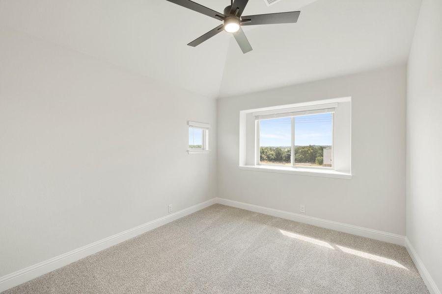 Empty bedroom with vaulted ceiling, ceiling fan, carpet flooring, and two windows with outdoor views