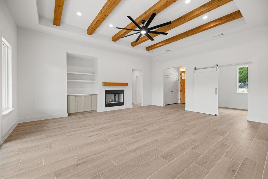 Exposed wood beams adorn the ceiling, complemented by recessed lighting and a sleek ceiling fan.