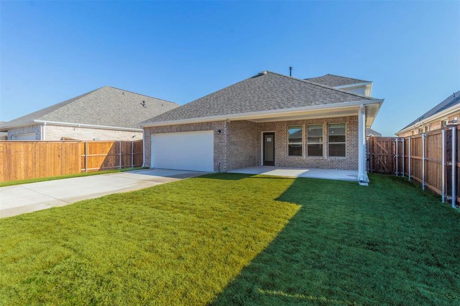 Rear view of property featuring brick siding, concrete driveway, a patio area, a shingled roof, and a fenced backyard