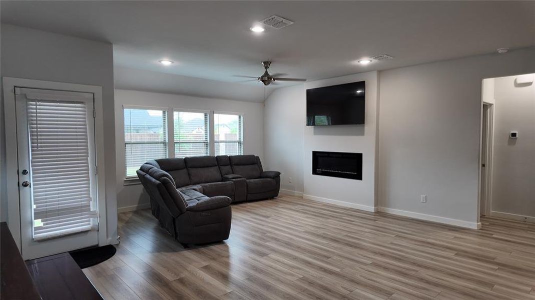 Spacious living area featuring light wood-look flooring, recessed lighting, and a modern wall-mounted fireplace