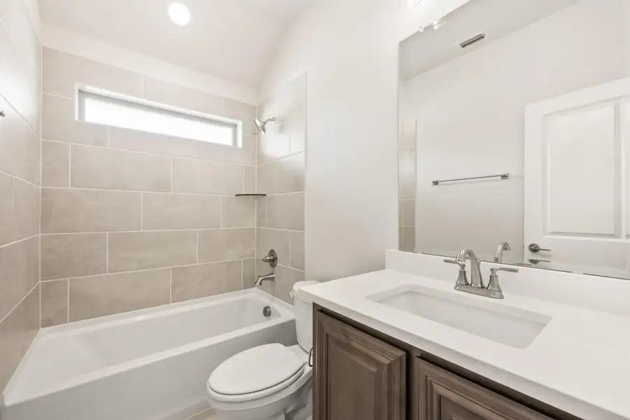 Bathroom with tiled tub surround, white countertop vanity, and large mirror