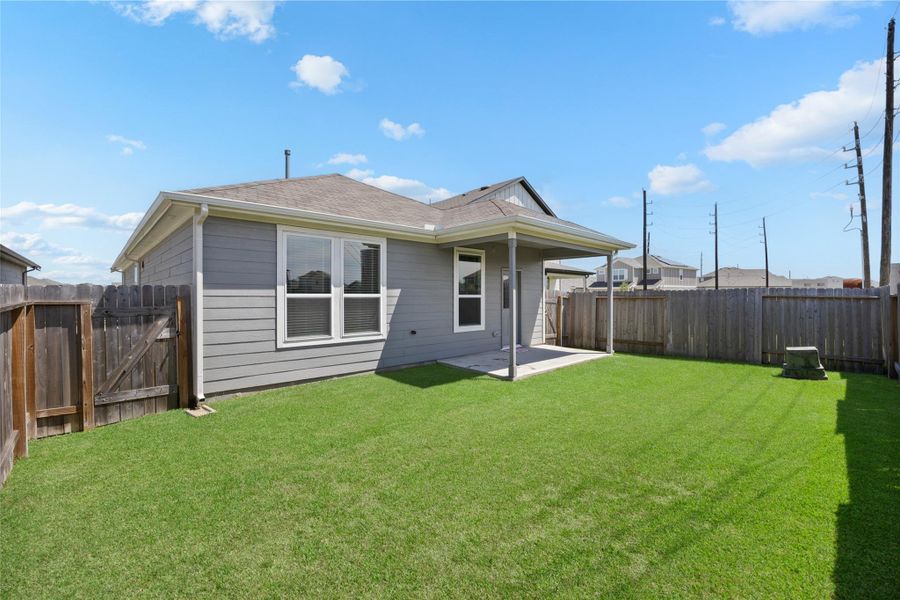 single-story home with a neat backyard featuring a lush green lawn and a small covered patio. The area is enclosed by a wooden fence, offering privacy and a cozy outdoor space.