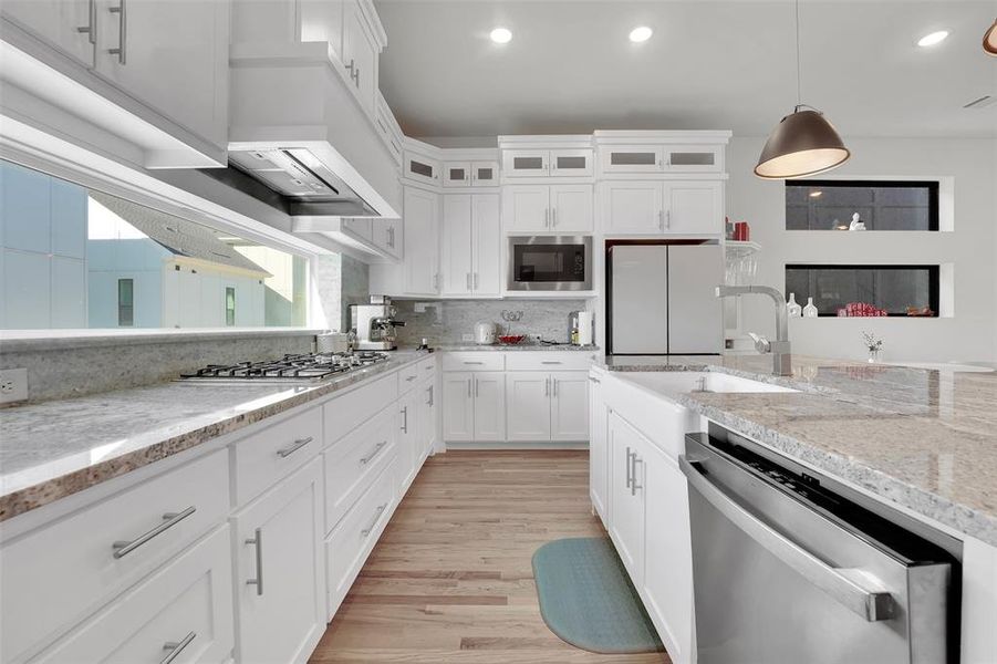 Kitchen featuring appliances with stainless steel finishes, light stone counters, light hardwood / wood-style floors, white cabinetry, and hanging light fixtures