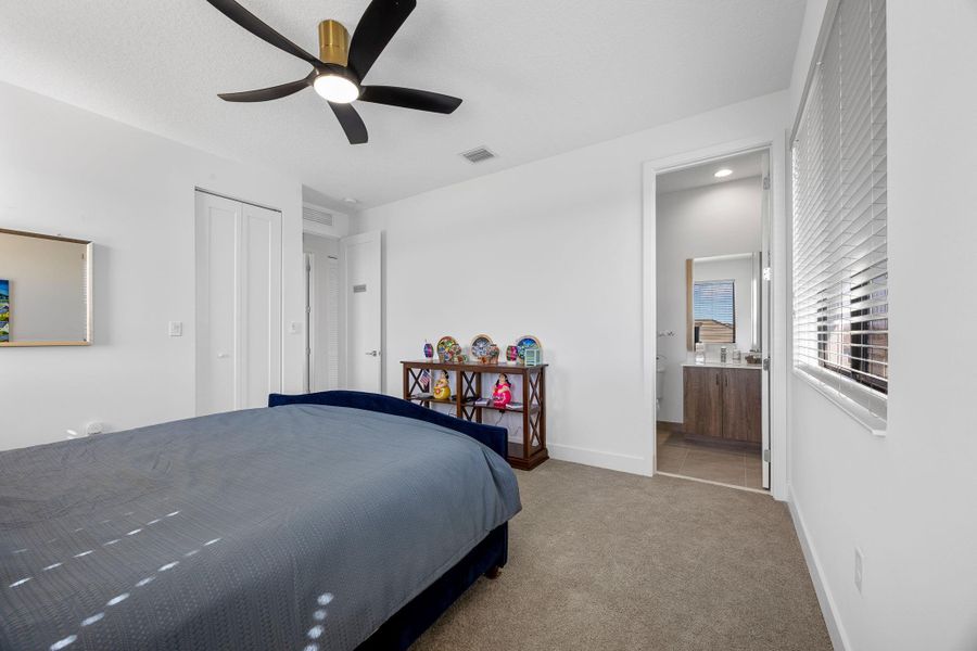 Carpeted bedroom featuring a ceiling fan and ensuite bath