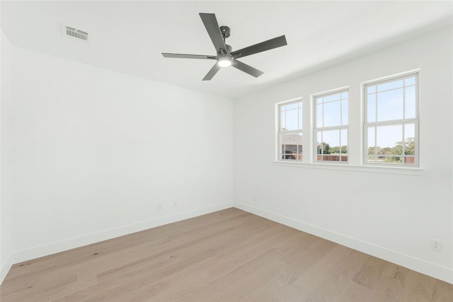 Empty room with light wood floors, ceiling fan, and three windows with natural light Empty room with light wood floors, ceiling fan, and three windows with natural light