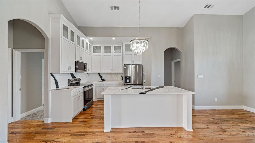 Kitchen featuring stainless steel appliances, arched walkways, light wood-style floors, and decorative backsplash