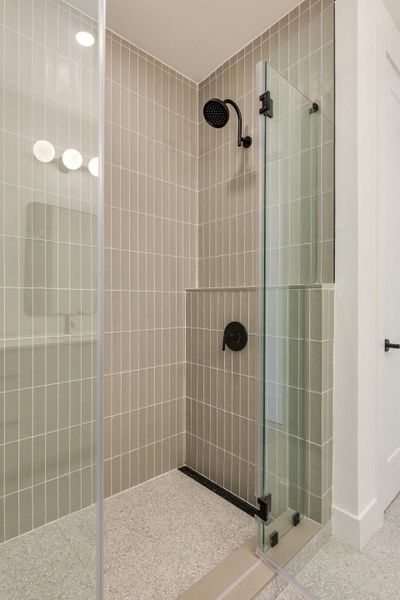 The shower features vertical tile walls, a rain showerhead, and a glass enclosure with matte black hardware