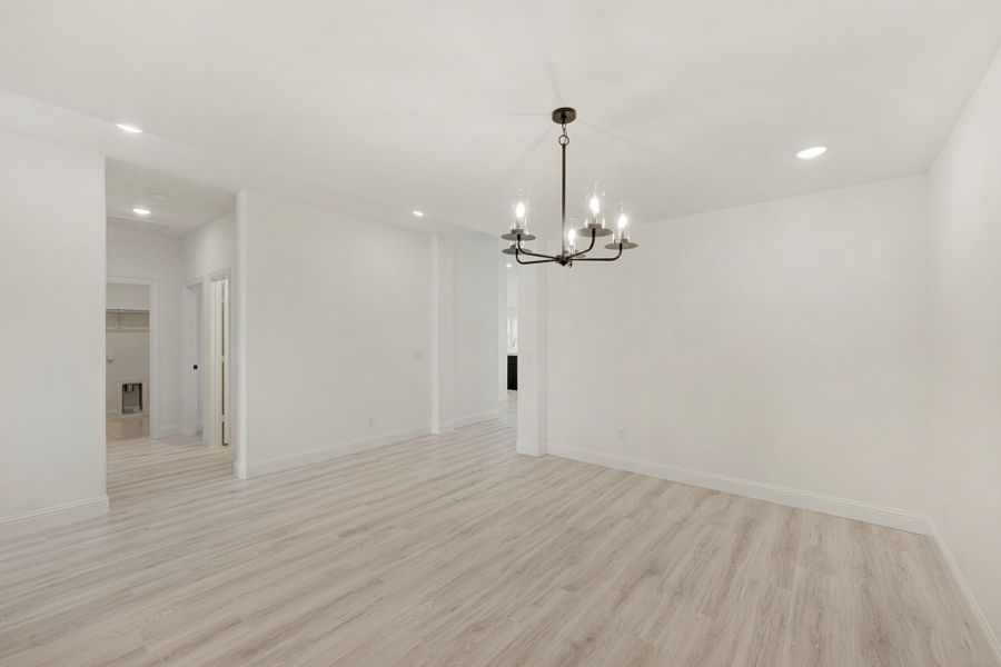 Empty dining room with light wood floors, white walls, and a black chandelier