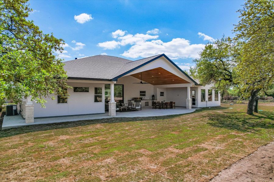 Back of property with a lawn, a patio, a shingled roof, and stucco siding
