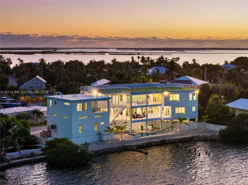 Multi-level waterfront residence featuring a rooftop deck, exterior staircase, ground-level pool, and stone-reinforced shoreline Multi-level waterfront residence featuring a rooftop deck, exterior staircase, ground-level pool, and stone-reinforced shoreline