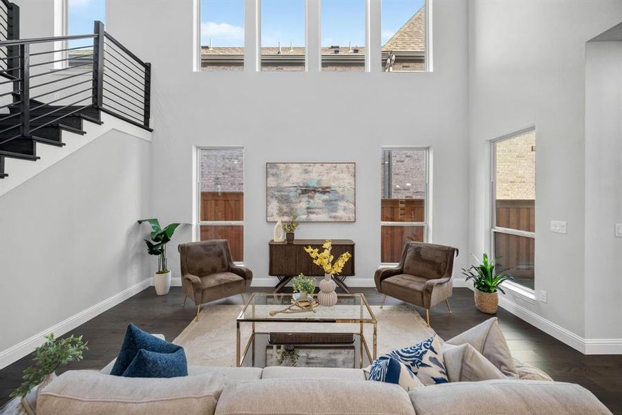 Vaulted ceiling living room featuring a contemporary open-tread staircase with black metal railings, wood-finish flooring, and multiple large windows providing ample natural light