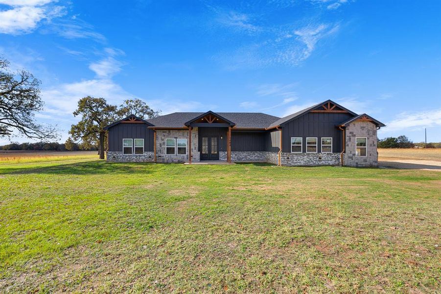 Modern farmhouse with board and batten siding, stone siding, and a front lawn