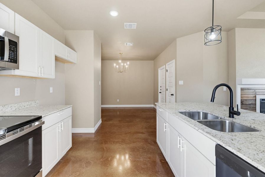 Kitchen featuring concrete floors, stainless steel appliances, white cabinetry, light stone counters, and a fireplace