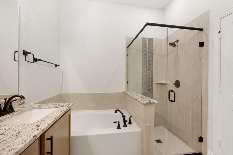 Bathroom with soaking tub, glass walk-in shower, tile walls, and granite vanity countertop with dark fixtures