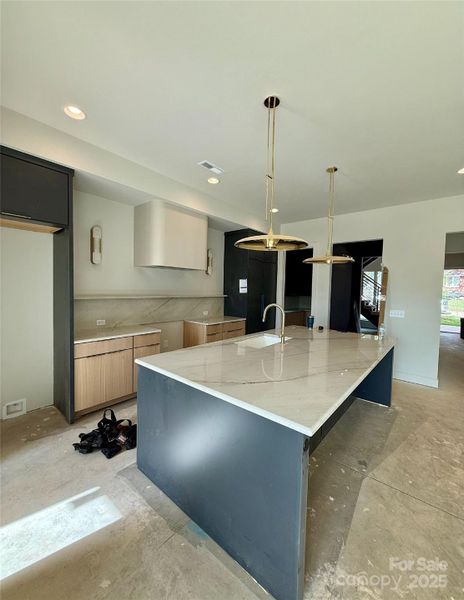 Kitchen with quartzite countertops and countertop backsplash, custom hood surround, custom cabinetry, designer lighting, oversized island