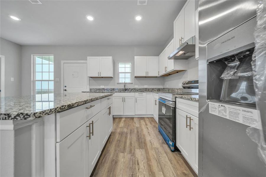 Kitchen featuring extractor fan, white cabinetry, stainless steel appliances, light stone countertops, and light wood-type flooring